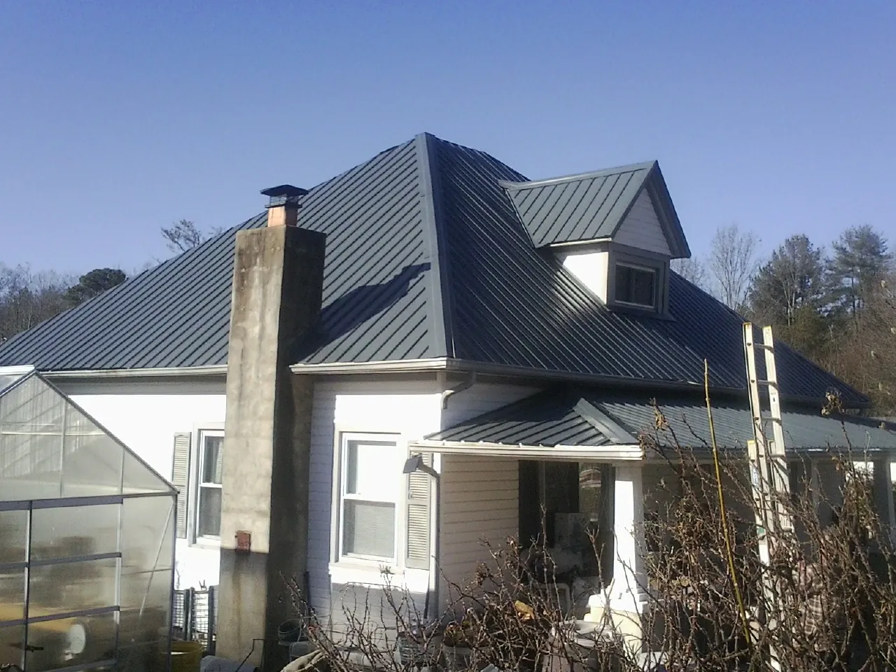 Dark blue standing seam metal roof on a white farmhouse with dormer — Slate & Tile Roof Repair by Roofing Brothers in Rimrock