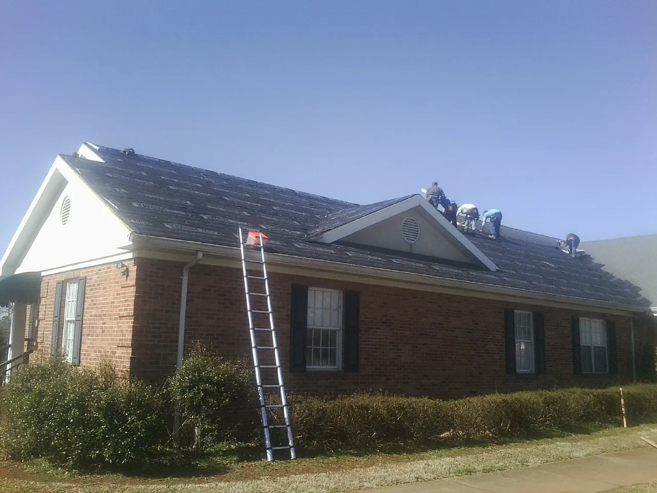 Crew tearing shingles off a brick ranch roof with a ladder set — Metal Roof Repair work by our crew in Rimrock