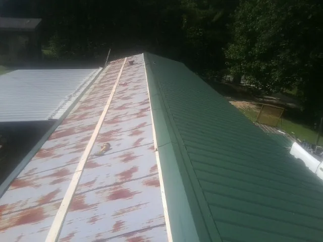 Old rusted panels beside newly installed green metal roofing — Wind Damage Roof Repair by Roofing Brothers in Rimrock