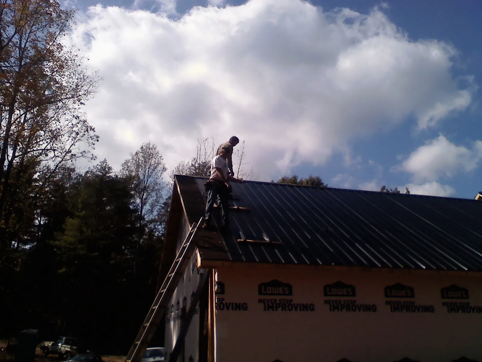 Roofer fastening dark metal panels high against a cloudy sky, from a Roof Inspection job in Rimrock
