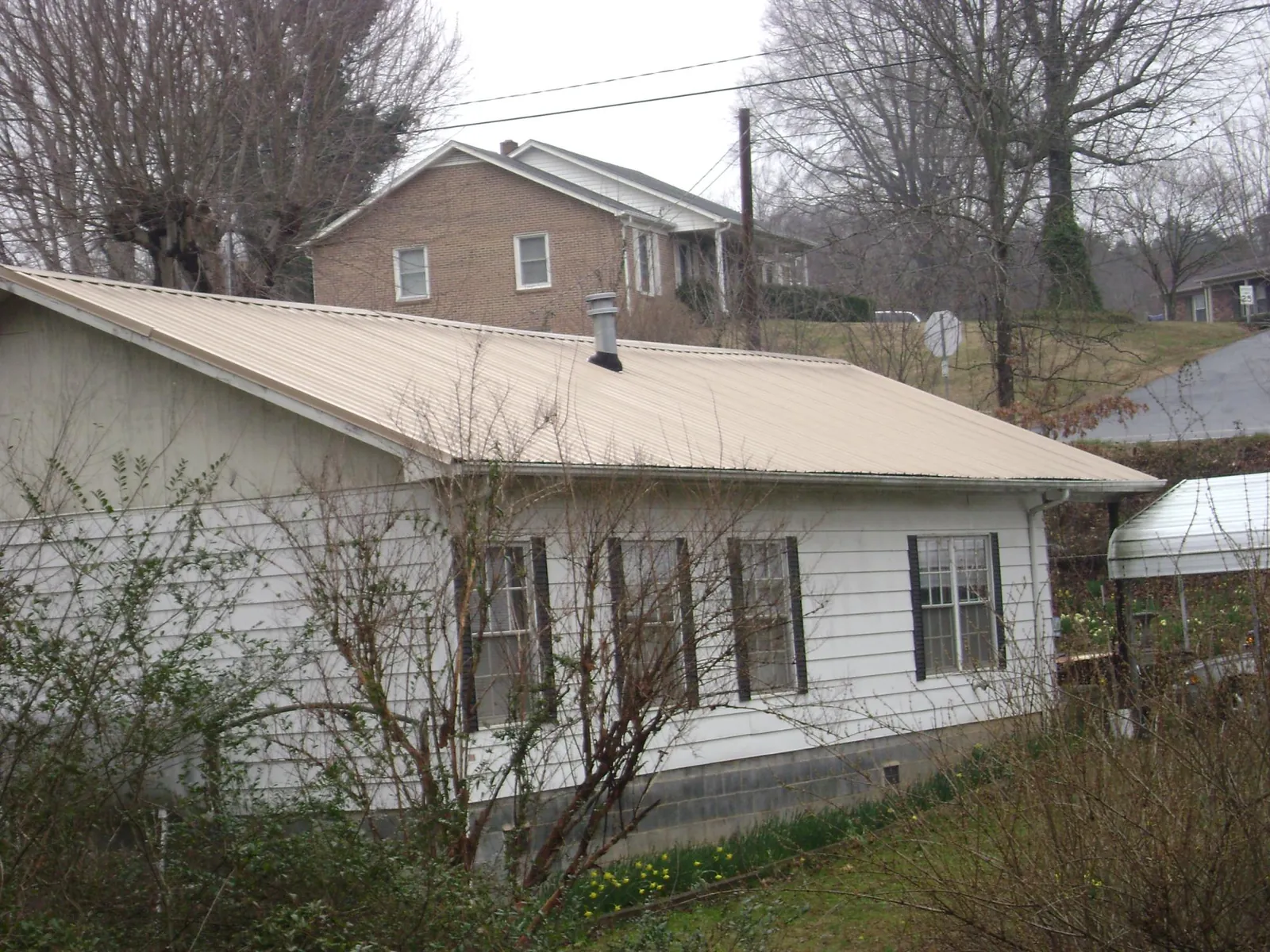 Tan metal roof on a white sided house set into a hillside — Commercial Roofing by Roofing Brothers in Rimrock